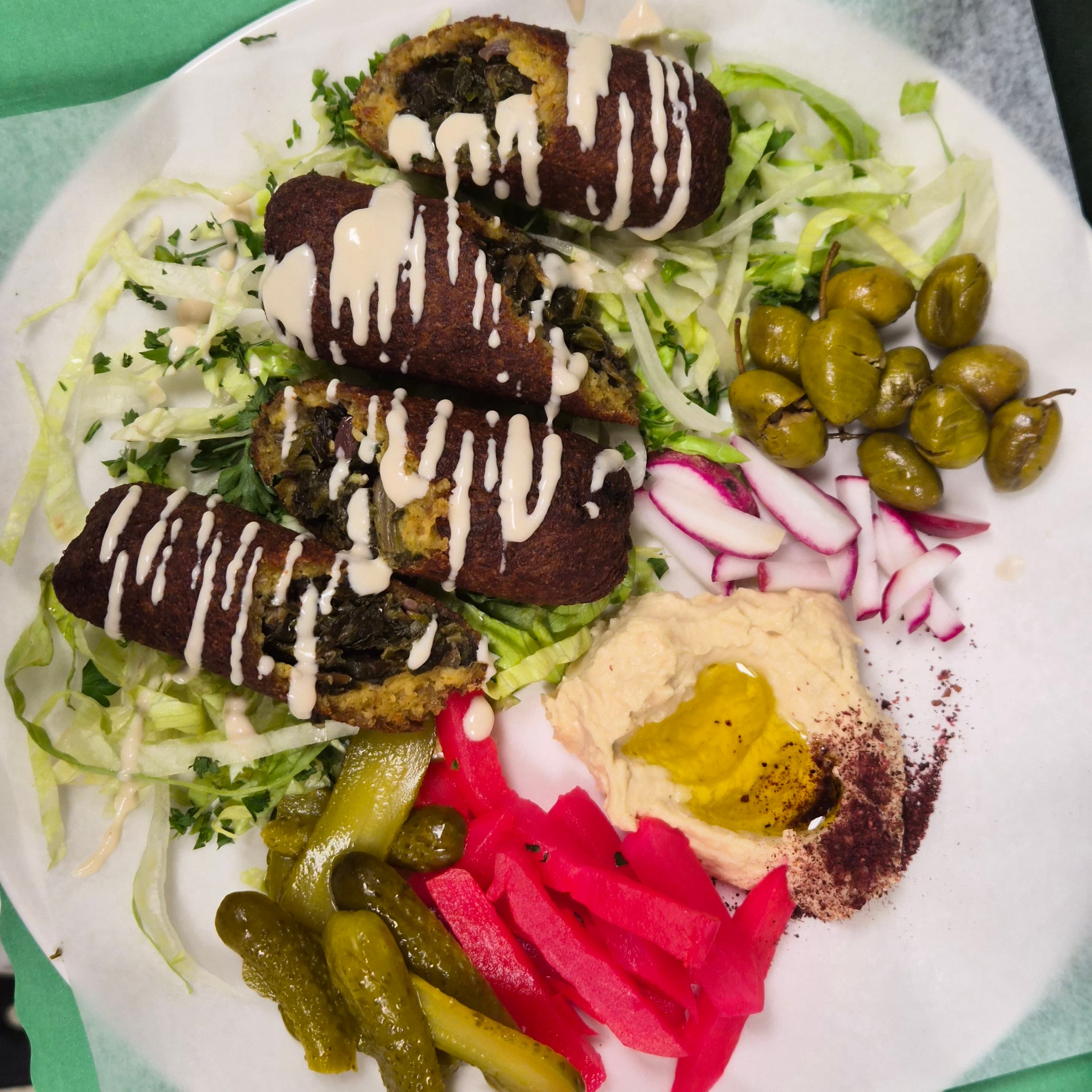 Stuffed fried rolls with tahini, hummus, olives, and pickled vegetables on a bed of lettuce.