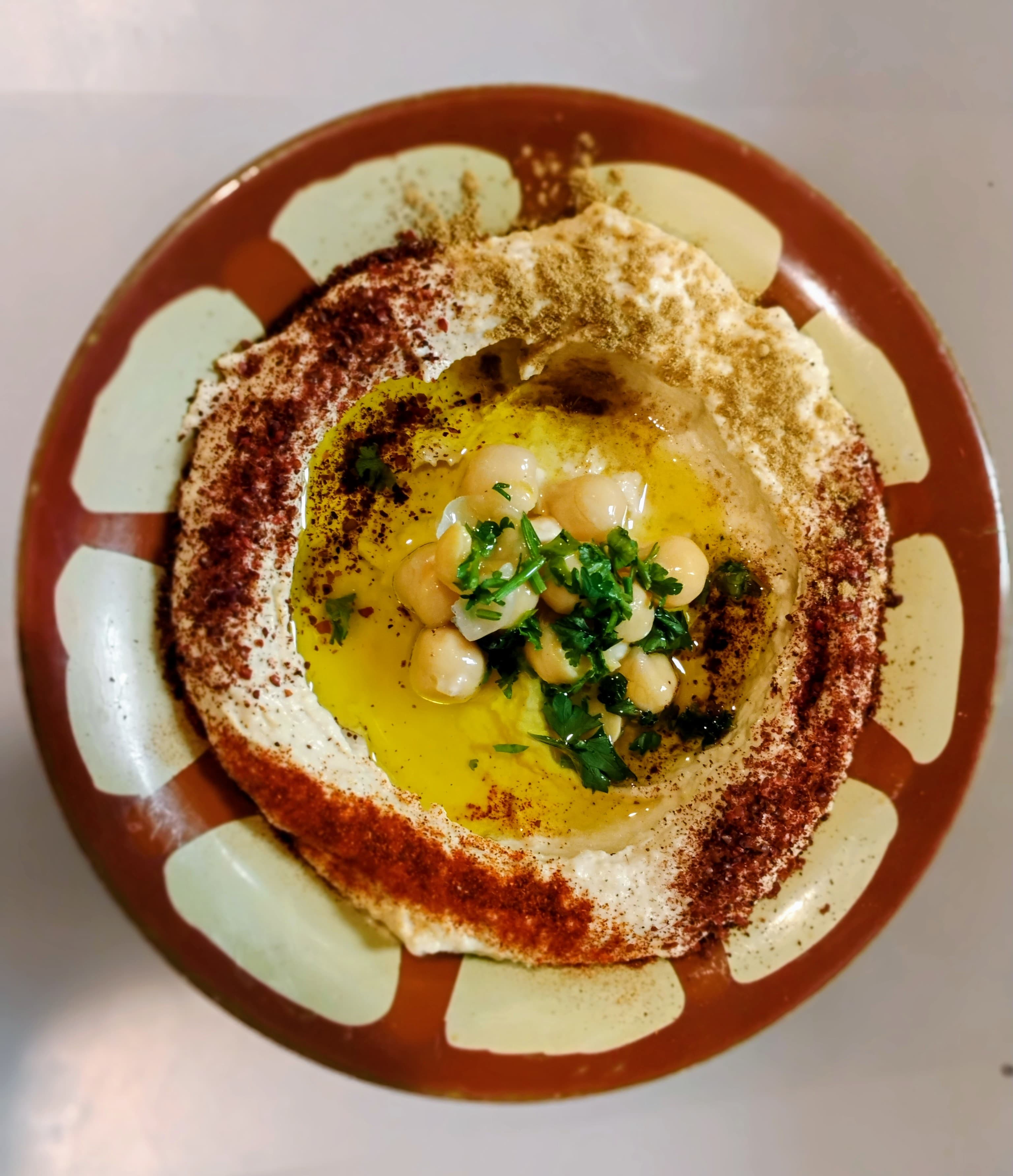 Hummus bowl topped with olive oil, whole chickpeas, fresh parsley, paprika, and cumin.