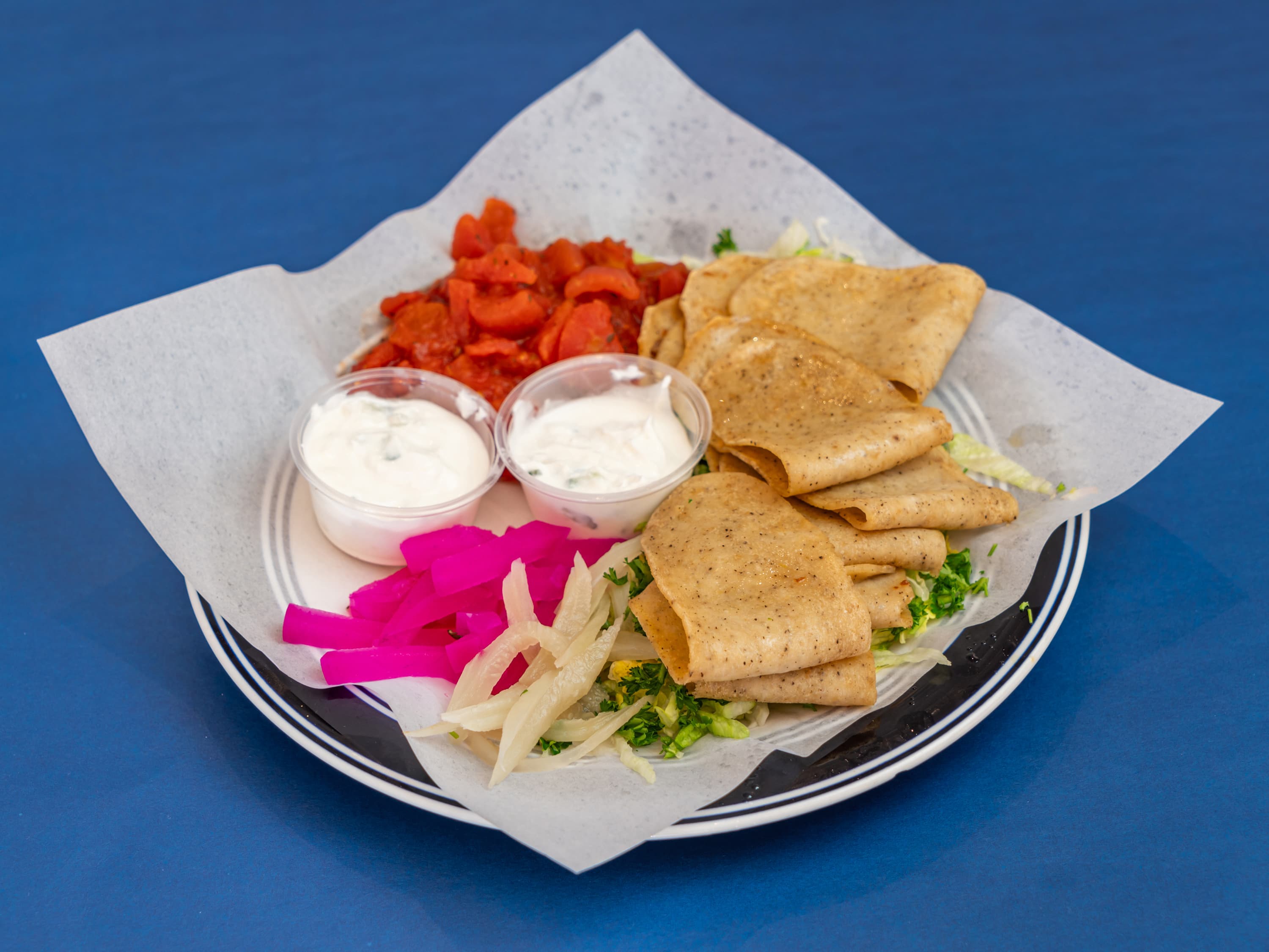Gyro meat platter with diced tomatoes, white sauces, pickled turnips, and onions on a plate.