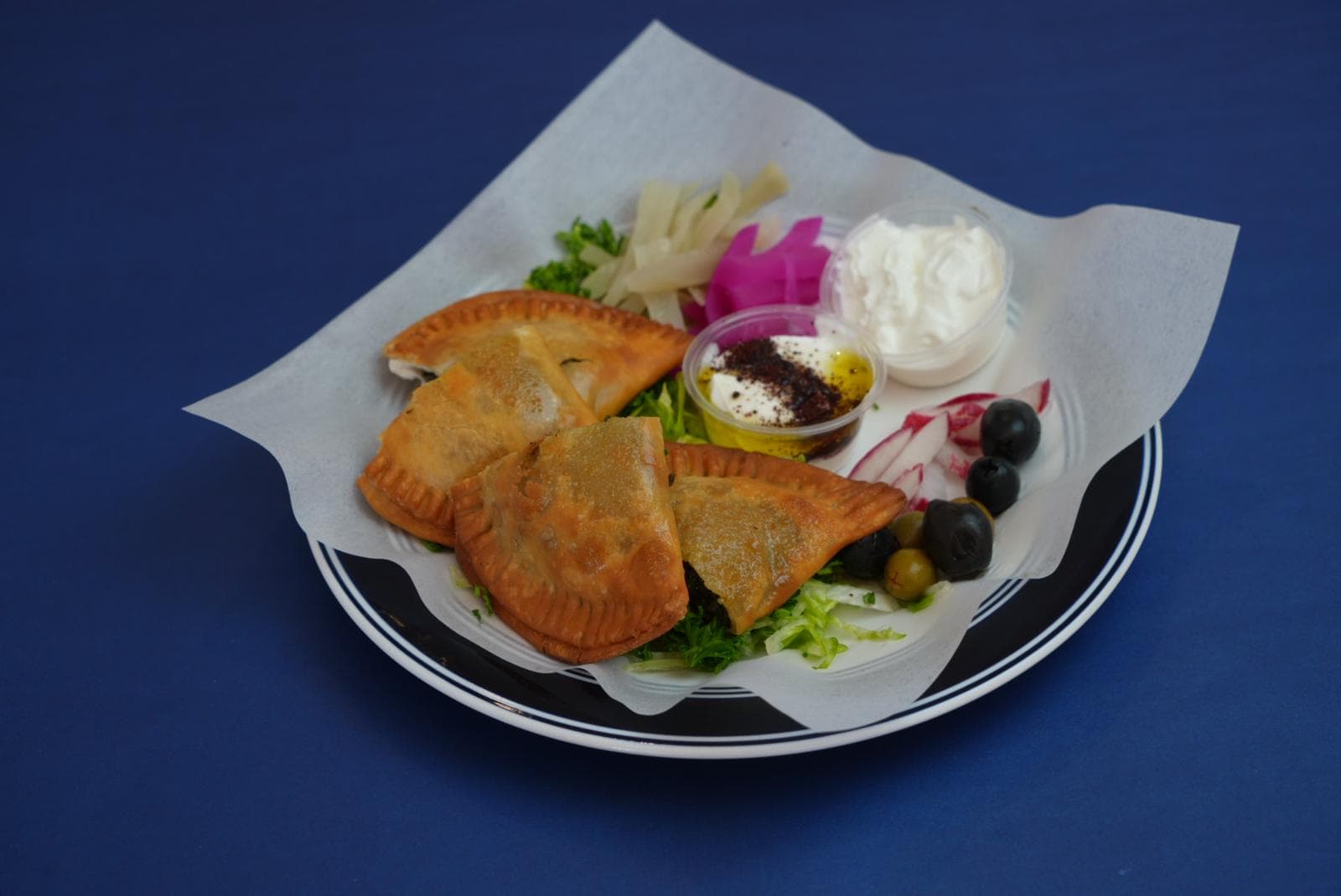 Golden fried pastries served with olives, pickled vegetables, and creamy dips on a plate.