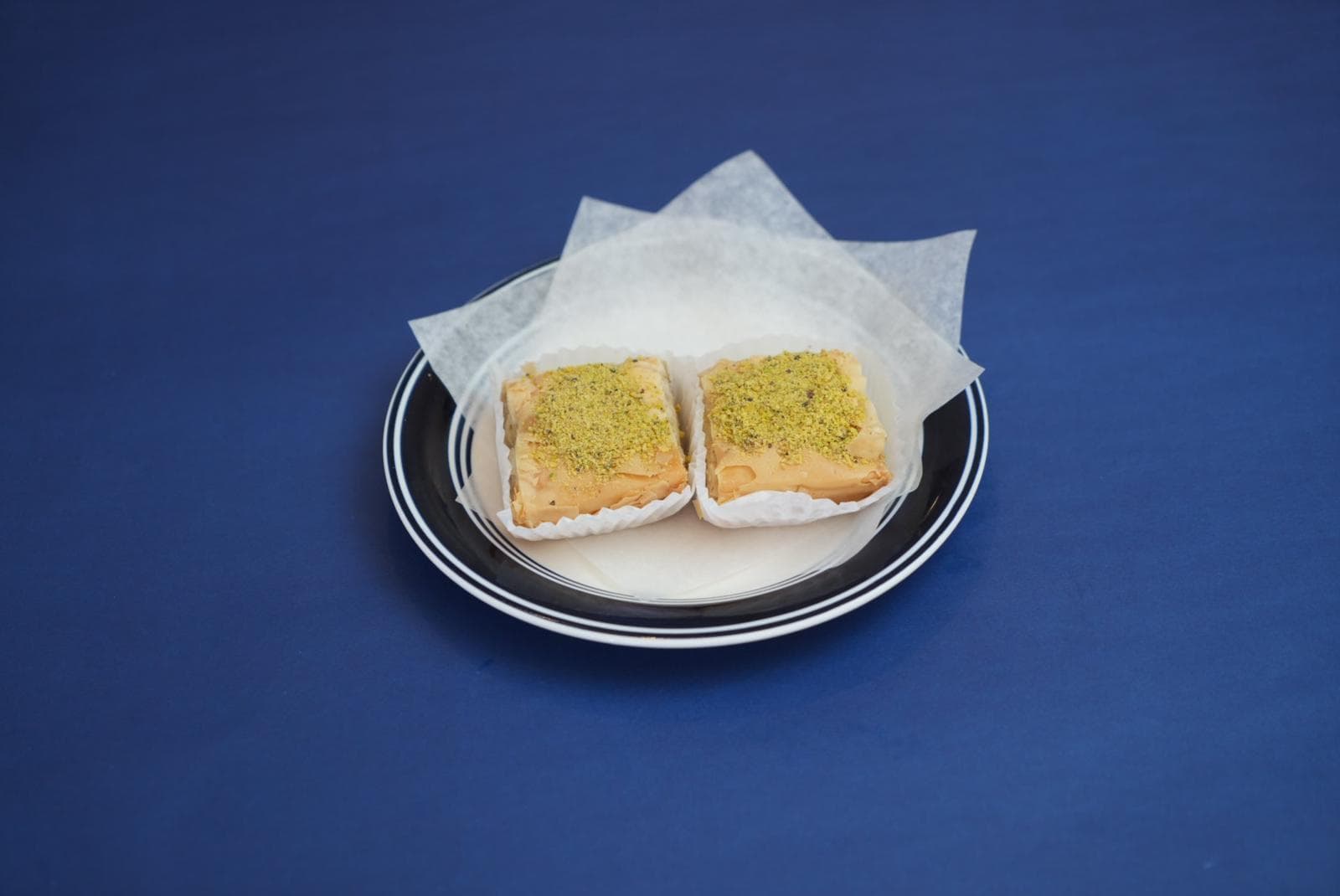 Two square pieces of baklava topped with crushed pistachios on a small striped plate.