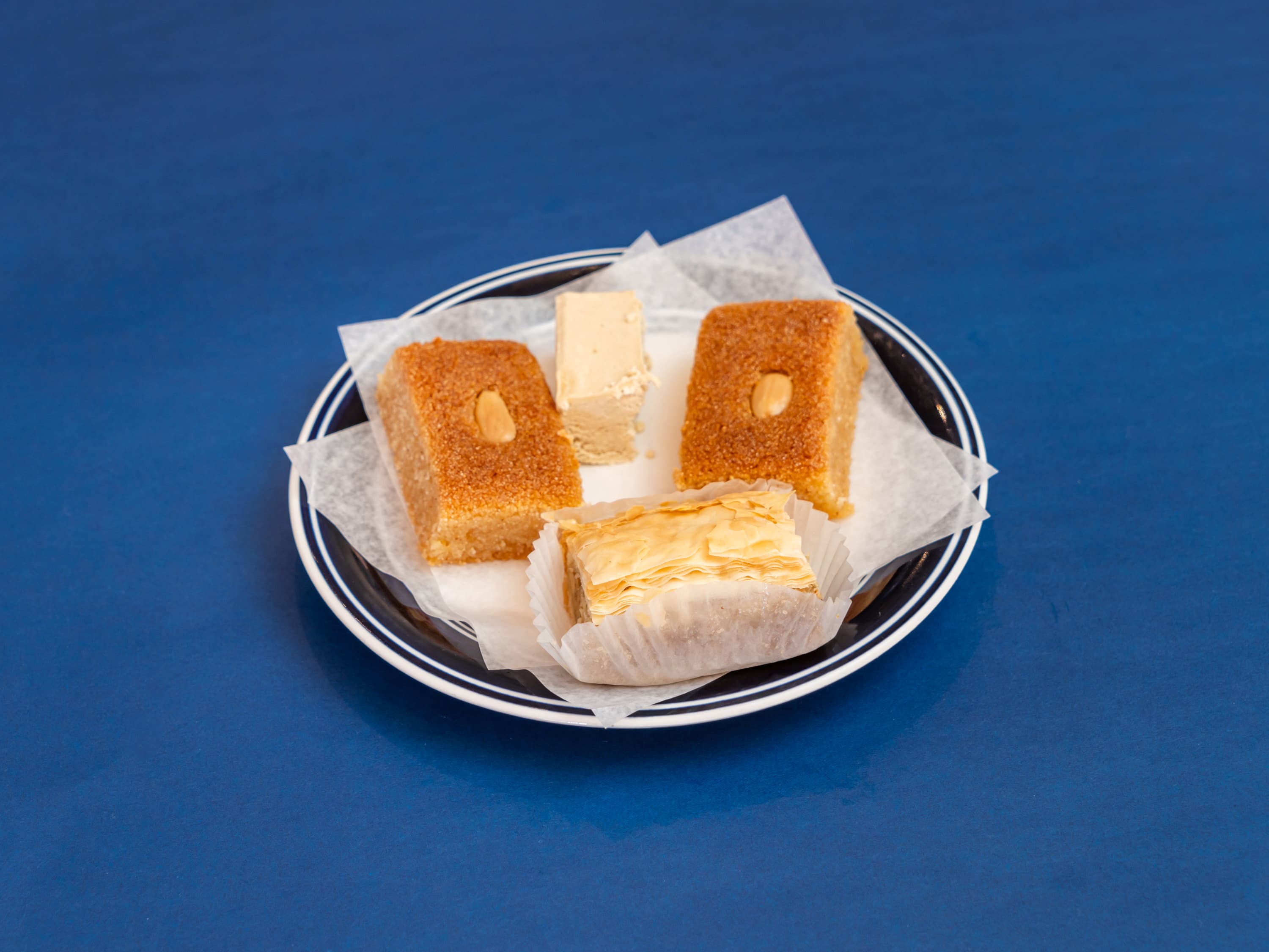 Plate of assorted Mediterranean pastries including baklava and semolina cake on a blue background.